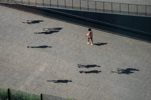 girl walking alone in street, with the shadows of other people present but not their bodies
