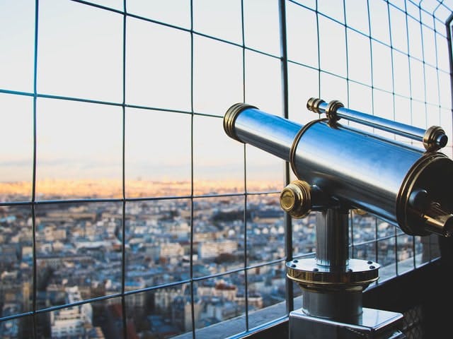 a telescope pointed out over a city through metal wire fence