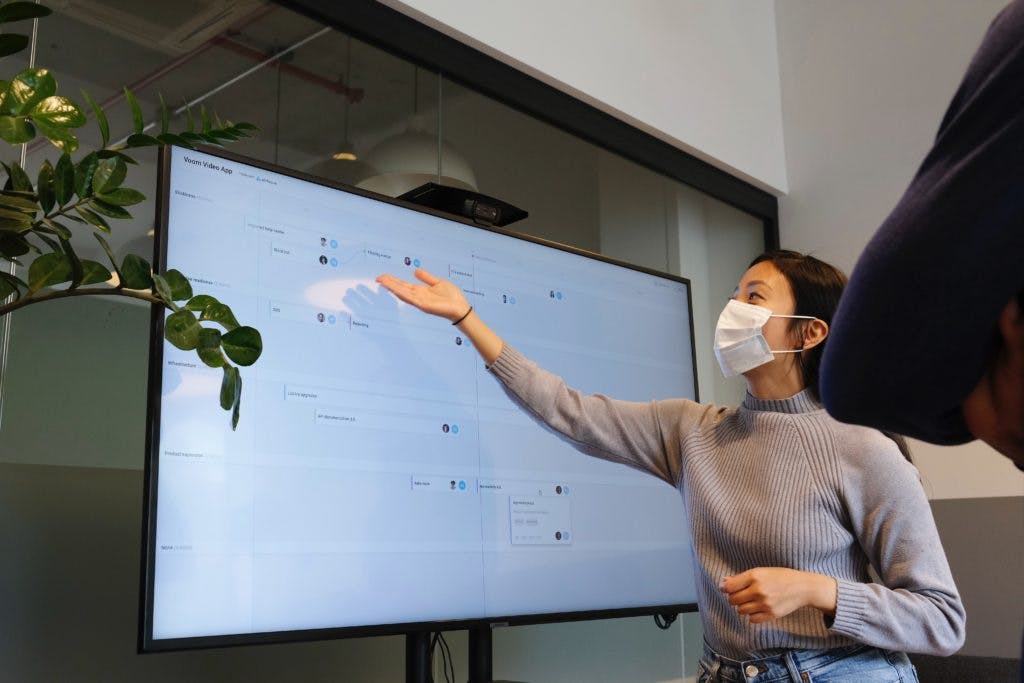 Person with mask pointing at screen 