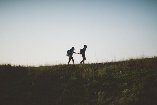 silhouettes of two people walking in the wilderness, one leading the other
