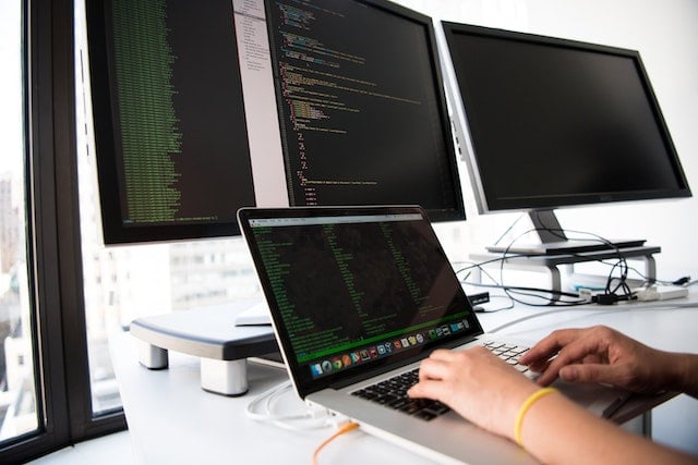 four computer screens and hands typing code
