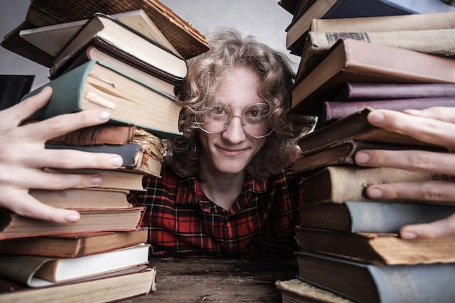 Person looks into camera as they hold two stacks of books, one on either side