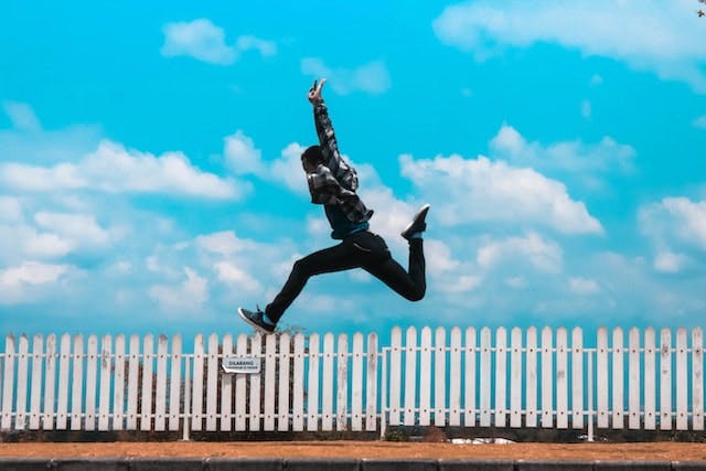 person jumping with white fence and blue sky in background