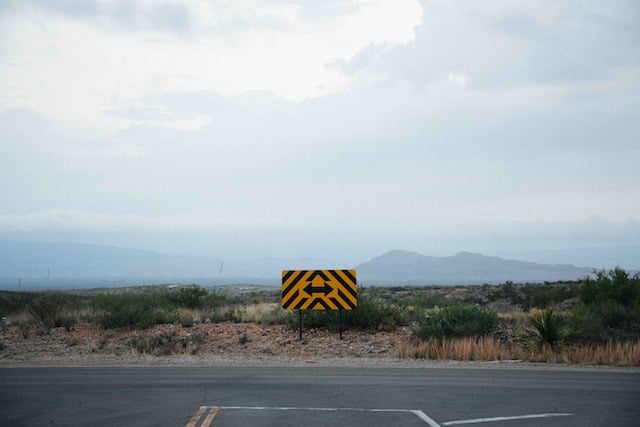 a turn sign pointing in two directions on a road. there are mountains in the haze in the background