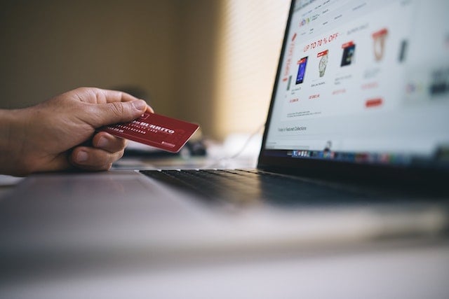 laptop screen out of focus, with a hand in the background holding a credit card