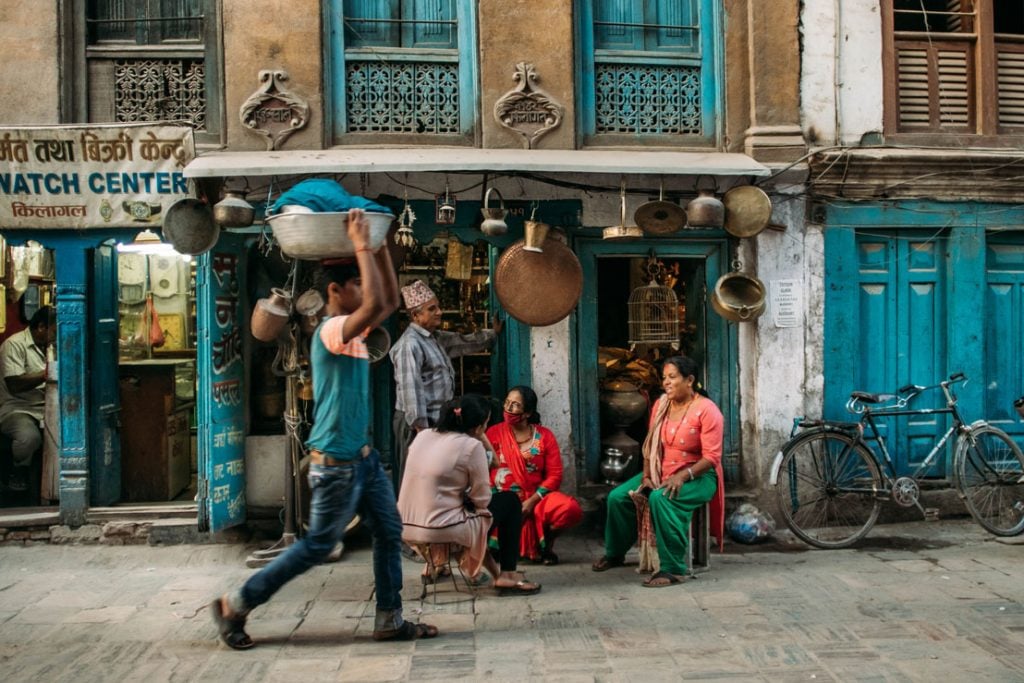 busy street with man carrying things on his head and people sitting down