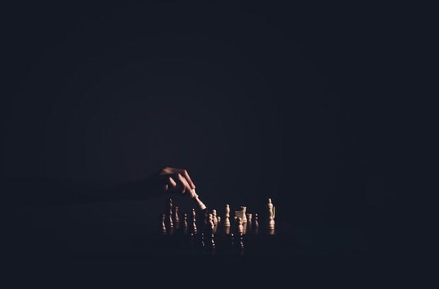 dark room. a light is on a hand, which move a piece on a chess board