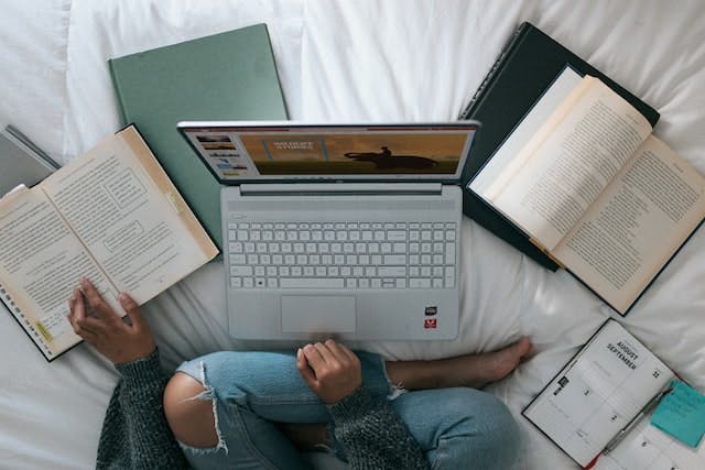 bird's eye view of someone seated on a bed with several books and a laptop open
