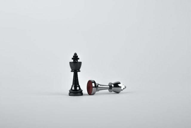 Two chess pieces against a white background. One piece is black, and standing. The other piece is silver, and on its side as though toppled over
