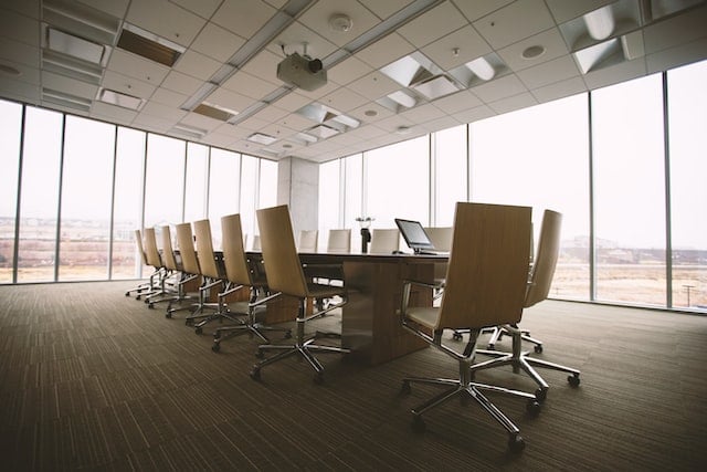 empty meeting room with wall-to-wall windows, a long table, and rows of rolling chairs