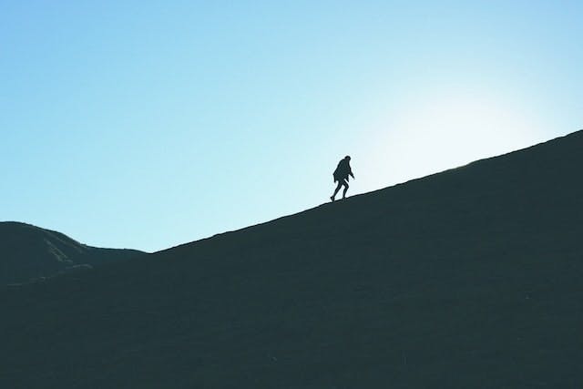 silhouette of a person in the distance climbing a hill. the sky is bright blue in the background