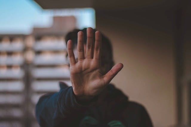 person with hand up to camera, covering their face. hand is in focus, body and background are out of focus