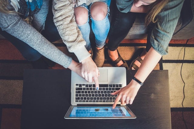 three people sitting around a computer pointing at the screen