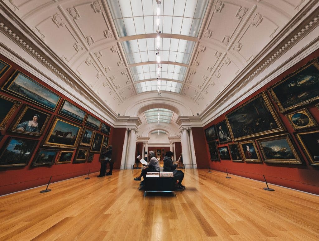 museum room with old paintings and people sitting down