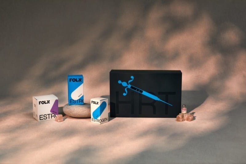 image of the folx estrogen hormone kit - there are 4 boxes total. two small blue and white ones, one small purple and white one, and one large black one with a blue needle graphic on it