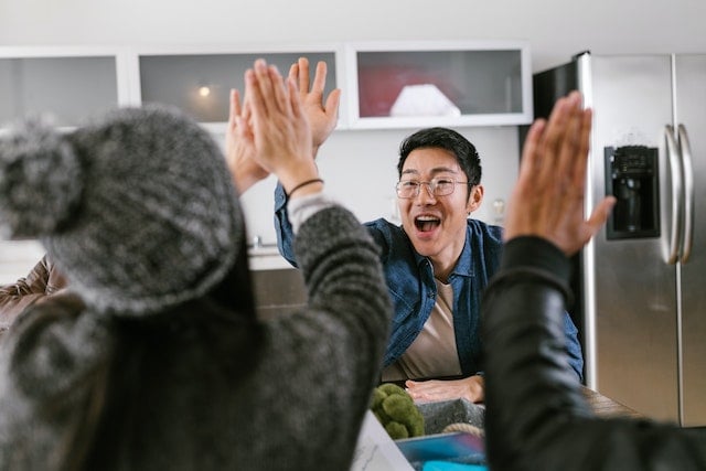 person giving high five to others seated around a table in a kitchen-office space