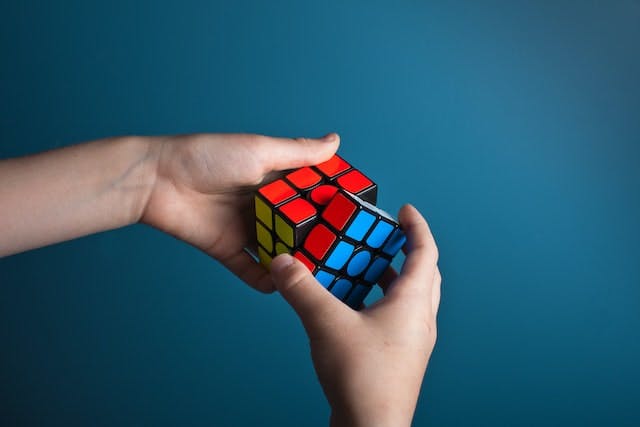 hands against blue background, holding an almost-solved rubix cube