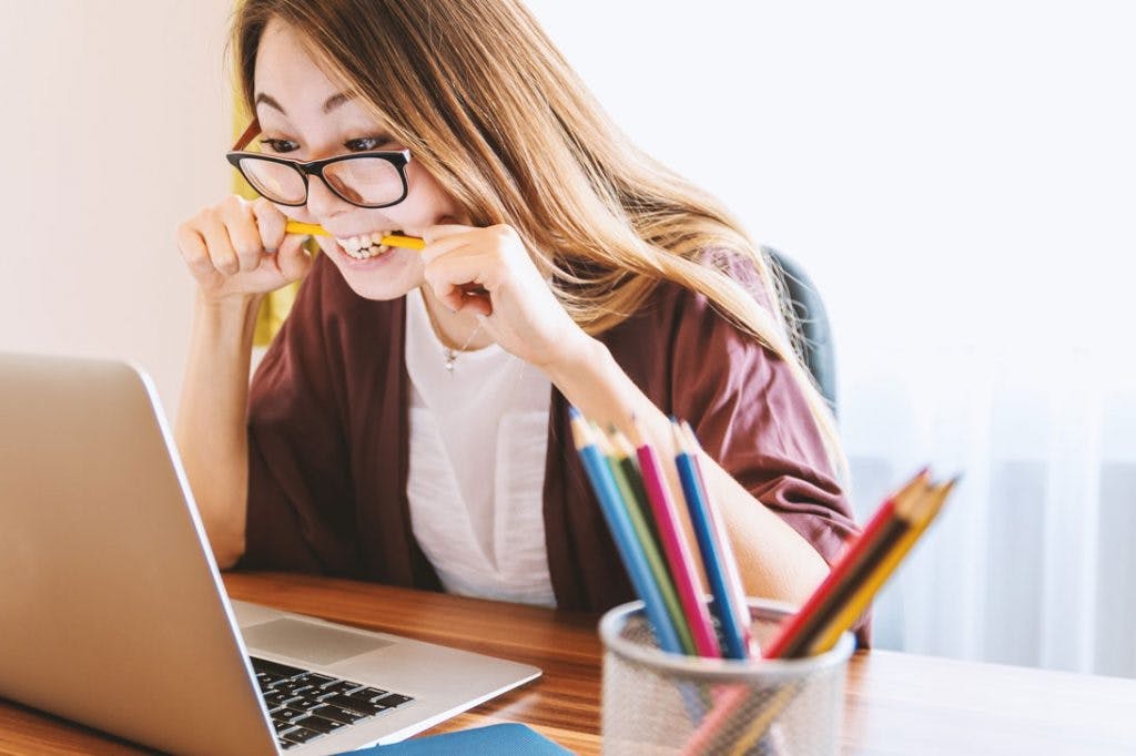 woman biting pencil sitting at desk in front of computer